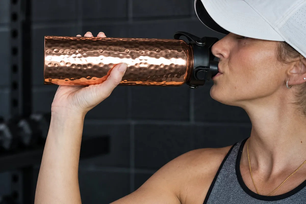 Woman drinking from the copper flip-top bottle at the gym